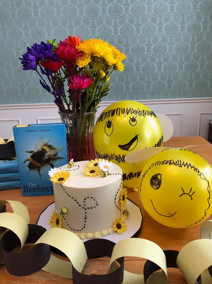 Bee balloons, a vase of flowers, a bee cake, and garland sitting on a table