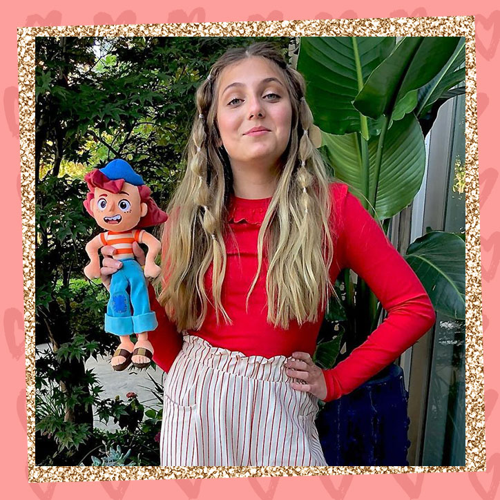 Actress Emma Berman poses in front of trees with a doll of Giulia, the character she voices in Disney Pixar's Luca