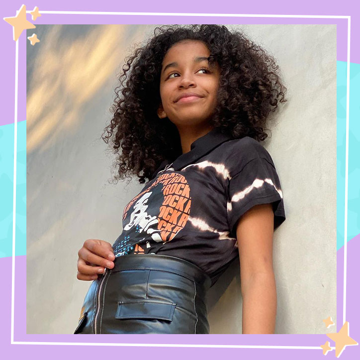 Actress Joryn Curet poses in front of a concrete wall with her hair down while wearing a rock tee and leather skirt