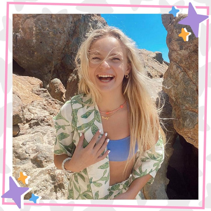 Pressley Hosbach laughs on the beach in a floral overshirt, shorts, and a blue bathing suit top
