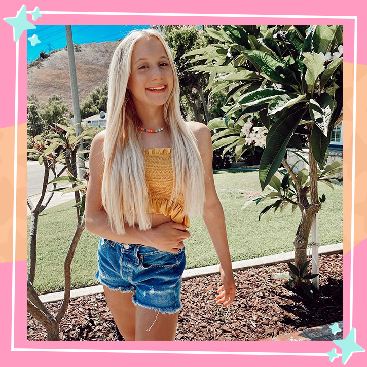 Dancer Katie Couch poses in front of palm trees while wearing a ruffled yellow tank top and shorts