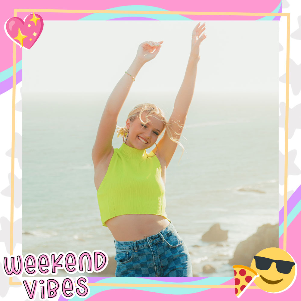 Indi Star smiles at the beach with her arms in the air while wearing a neon crop top and checkered jeans