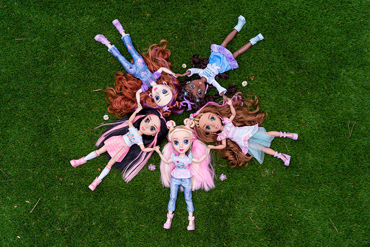 All five B-Kind dolls laying in the grass in a circle while holding hands