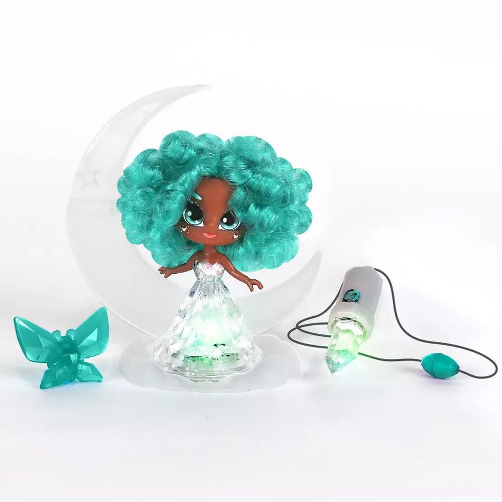 Turquoise Crystalina doll sitting on her crescent moon shaped base with a butterfly shaped hairclip and crystal amulet necklace