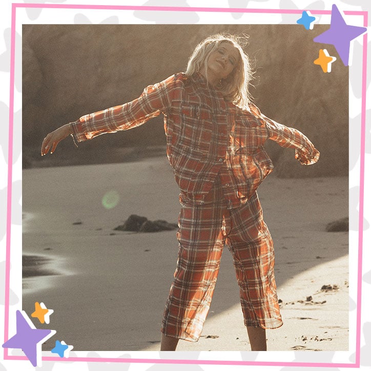 Indi Star poses on the beach in a flowy, burnt orange plaid pant suit