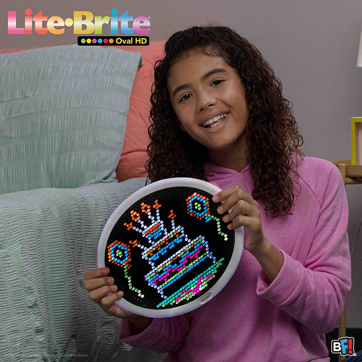 A tween girl holding up a design of a birthday cake and balloons she created on a Lite-Brite Oval HD