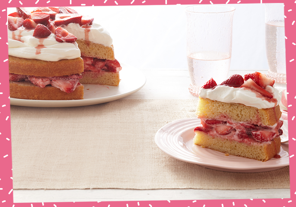 A strawberry shortcake layer cake sitting on top of a white plate on a tan placement, with a slice of the same cake off to the right on a similar plate.