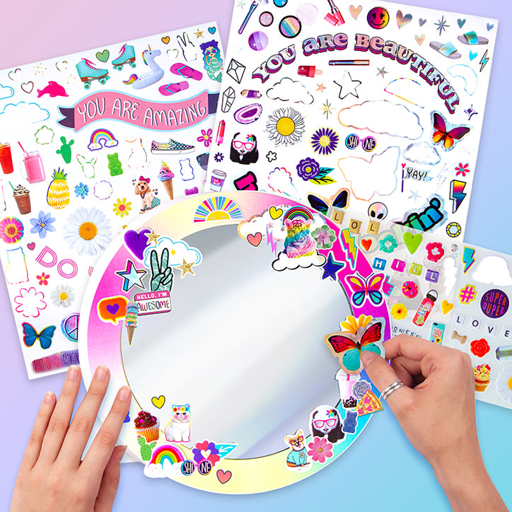 Flat lay of the Fashion Angels Sticker Collage Mirror Design Kit including two sticker sheets and a rainbow framed mirror