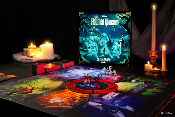 Product shot of the Disney Haunted Mansion: Call of the Spirits Game including box art, game board, and included pieces laid out on a table in a dim room with candles all around