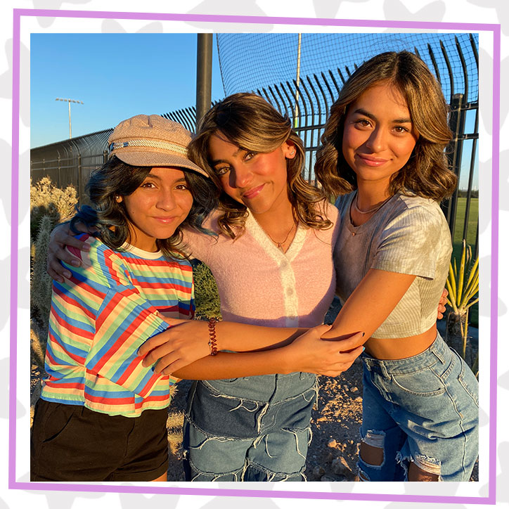 GEM Sisters Evangeline, Mercedes, and Giselle hugging outdoors as the sun sets in front of a fence