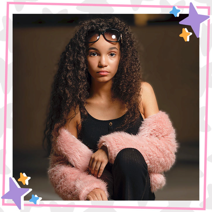 Kherrington Briggs poses with a fluffy pink faux fur coat wrapped around her arms over an all black outfit, sunglasses propped up on her head