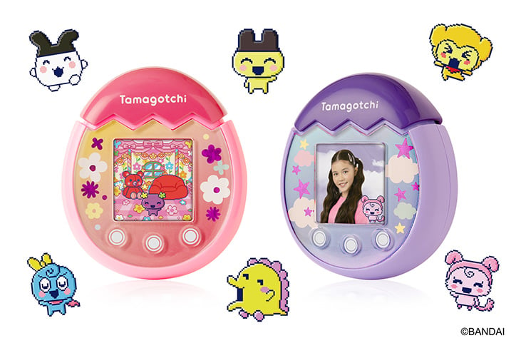 Two Tamagotchi Pix devices (Pink and Purple) side by side with Tamagotchi characters all around them