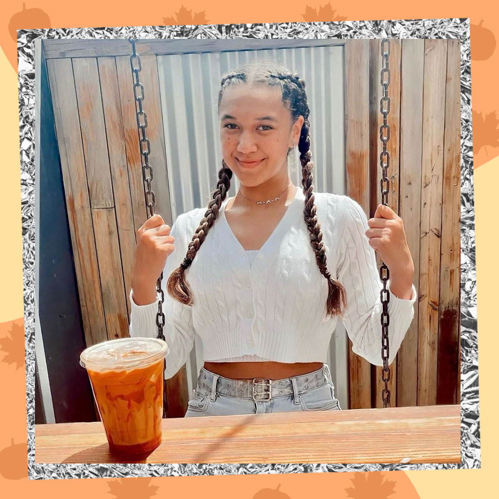 Keilahni Dixon poses on a swing in a cropped white cable-knit sweater and long braids. A pumpkin spice latte sits on the table in front of her.