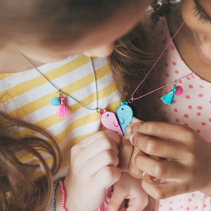 Downward shot of two girls holding their Calico Sun narwhal best friend necklaces together