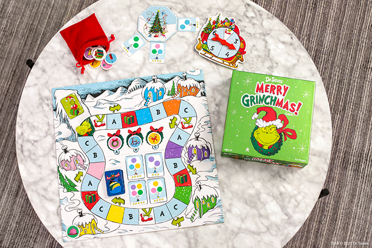 Flat lay of the Merry Grinchmas game, including the game box, game board, spinner, and tokens that come with the game