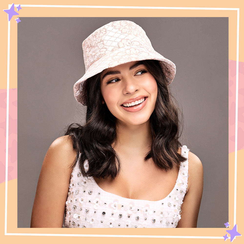 Kyndra Sanches poses in front of a gray backdrop while wearing a pastel pink bucket hat and rhinestone floral tank 