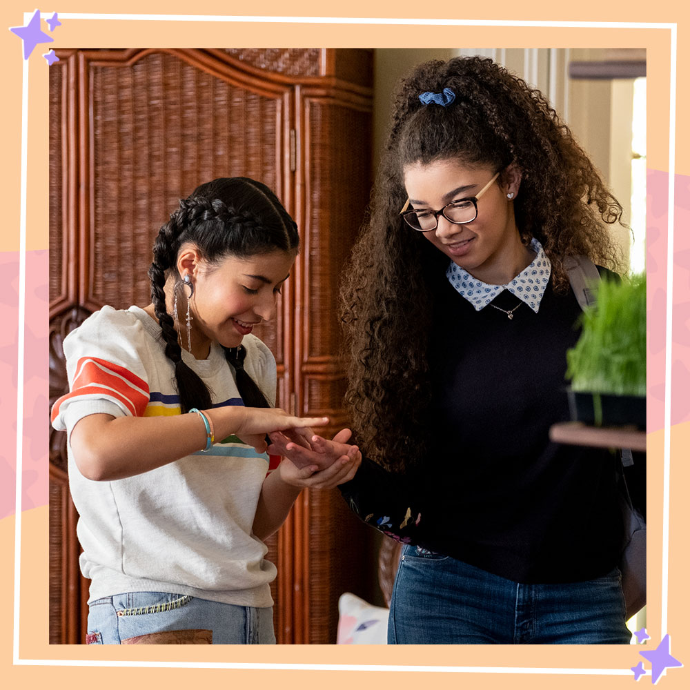 Photo from the set of The Baby-sitters Club featuring Kyndra Sanchez and Malia Baker in character as Dawn and Mary-Anne. Kyndra is reading Malia's palm.