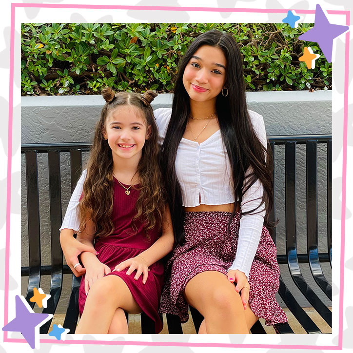 Jasmine and Bella Mir sit together on an outdoor bench. Jasmine has her arm wrapped around her sister Bella