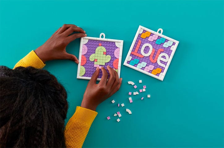 Lifestyle photo of kid creating their LEGO DOTS Message Board. They have created the two smaller frames, one has a cactus and one says LOVE