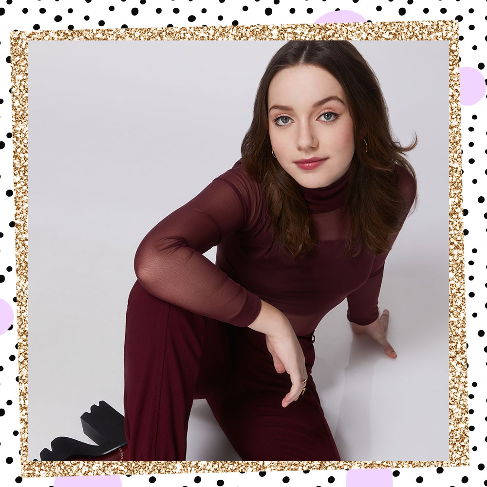 Image of Libby Rue sitting on the ground with her arm draped over her knee. She is wearing a sheer burgandy with cami underneath, burgandy dress pants, and chunky platform boots