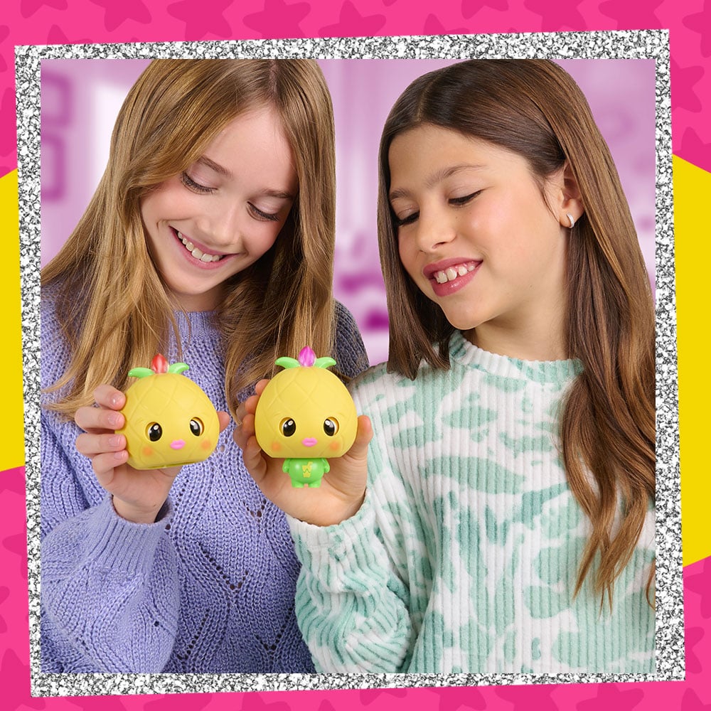 Lifestyle photo of two tween girls holding up the My Squishy Little Pineapple figure. One has the body popped out and the other is in it's pre-squished state.