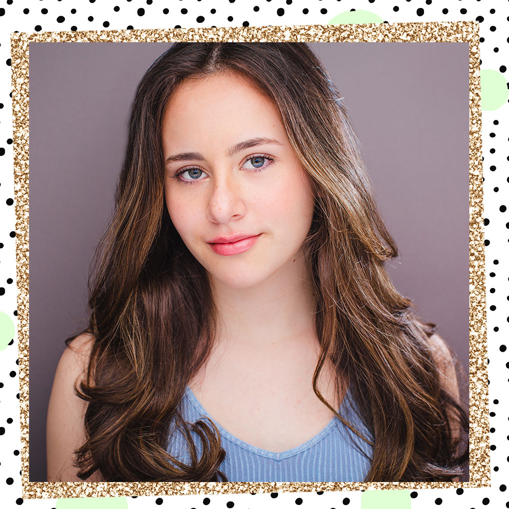 Abbie Grace Levi poses in front of a gray backdrop. Her long styled hair flows over her shoulders. She is wearing a periwinkle blue tanktop.