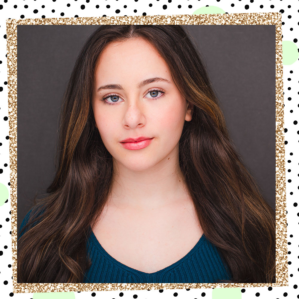 Abbie Grace Levi poses in front of a dark gray backdrop. Her long hair flows over her shoulders. She is wearing an emerald green top.