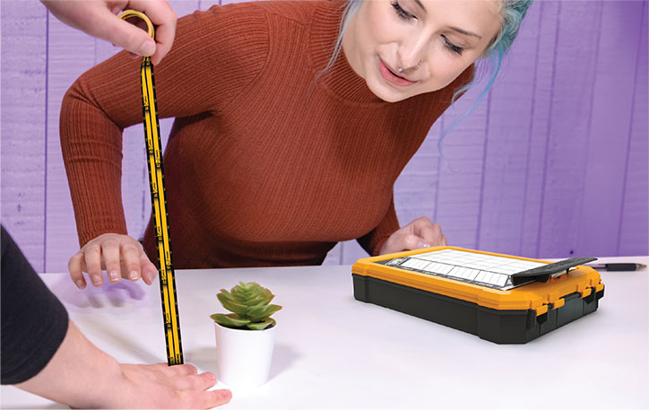 Lifestyle image of people playing the T.A.P.E.S. game, using one of the included measuring tapes to measure a succulent plant.