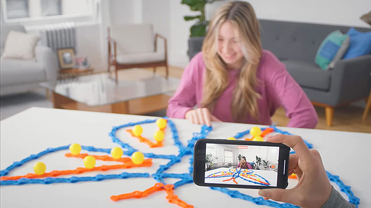 Lifestyle photo of a girl sitting at a table setting up a butterfly shaped ZipLinx run while someone films her with their phone