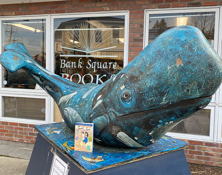 A copy of Sweet and Sour sits in front of a large whale sculpture in front of Bank Square Books, a location found in the book