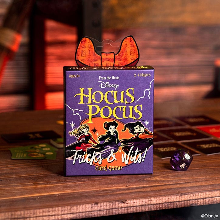 Lifestyle photo of the Hocus Pocus Tricks & Wits card game featuring the game box, cards, and dice sitting on a wooden table