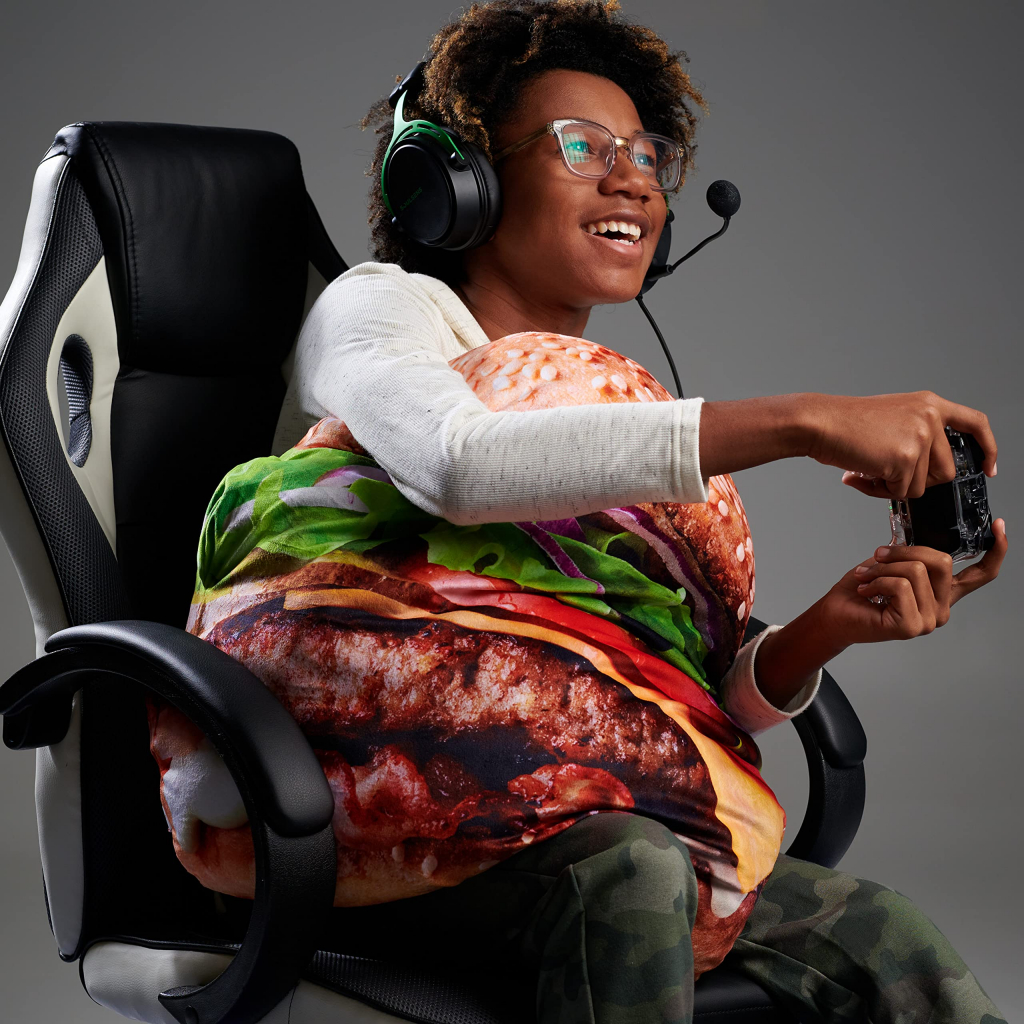 Teenager sitting in a gaming chair with a headset and game controller, snuggling a Seriously Supersized Cheeseburger Plush