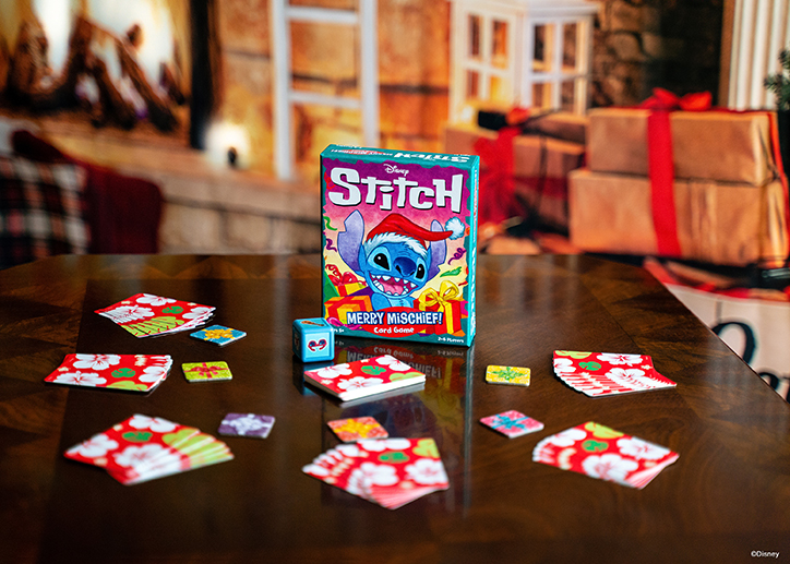 Lifestyle photo of the Disney Stitch Merry Mischief card game laid out on a table in front of a holiday decorated fireplace