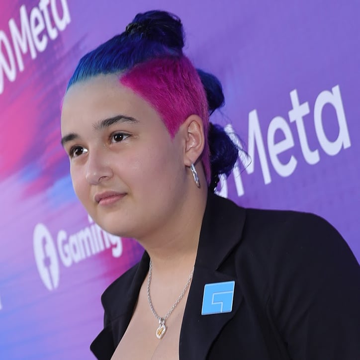 Streamer FabuRocks standing in front of a Facebook Gaming backdrop. She has pink and blue hair up in buns and is wearing a black blazer.