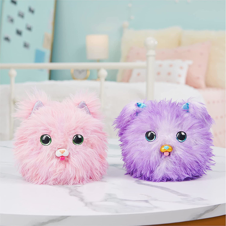 Lifestyle photo of two What the Fluff? interactive pets sitting side by side on a table in a bedroom