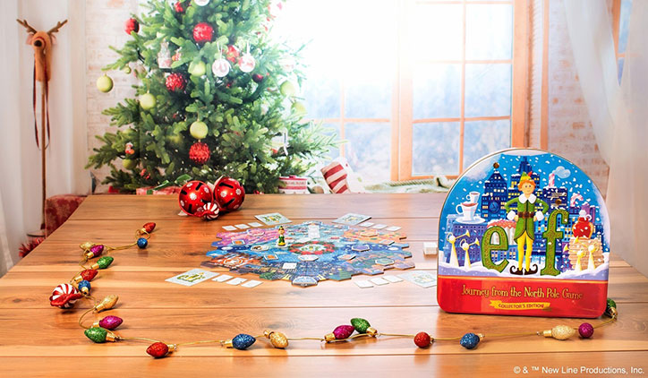 Lifestyle photo of the Elf: Journey from the North Pole: Collector's Edition board game set up on a living room table. There is a decorated Christmas tree in the background and ornaments scattered around the table.