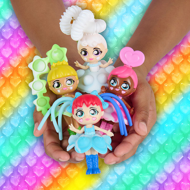 A girl holding out her hands with 4 Fashion Fidgets Rainbow Series dolls in front of a rainbow heart backdrop