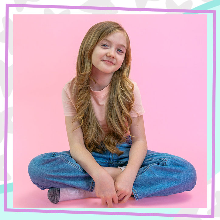 Lily, Founder of Lily Lou's Aromas sitting and smiling in front of a pink backdrop