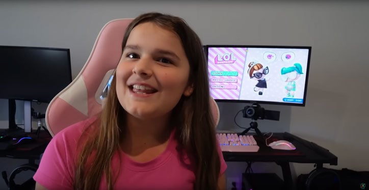 Maddy from JKrewGaming sitting in a pink and white gaming chair in front of her computer. On the desk is a pink gaming keyboard and mouse.