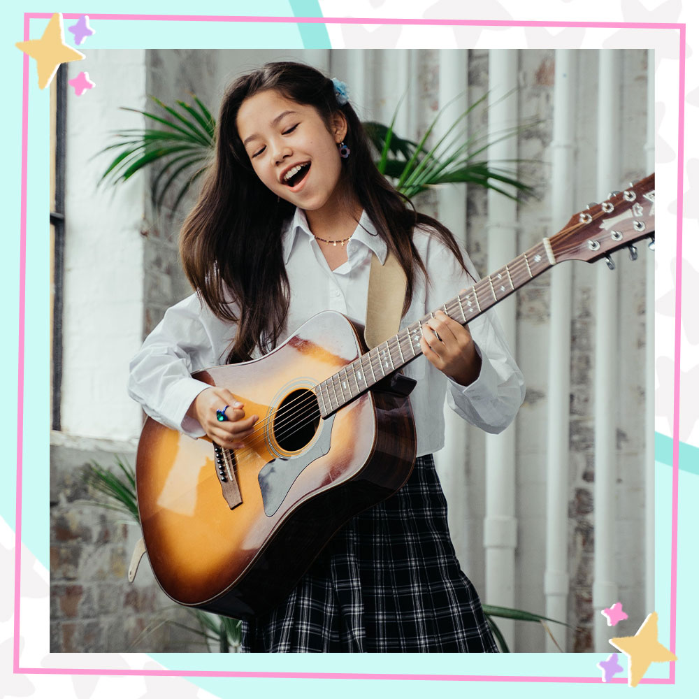 Trinity Jo-Li Bliss playing guitar in a school uniform inspired outfit