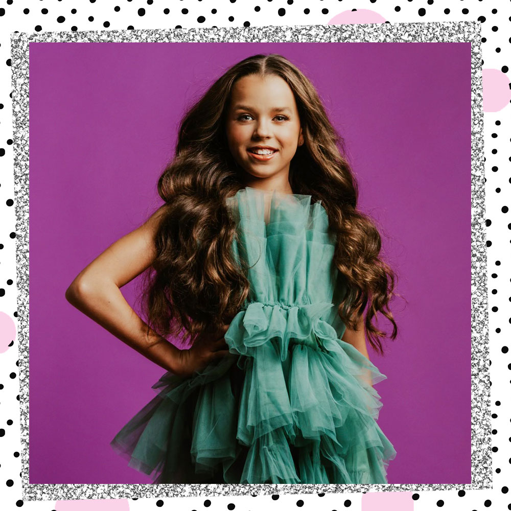 Tatum Brady stands in front of a purple backdrop with her hand on her hip. She is wearing a teal fluffy ruffled dress.