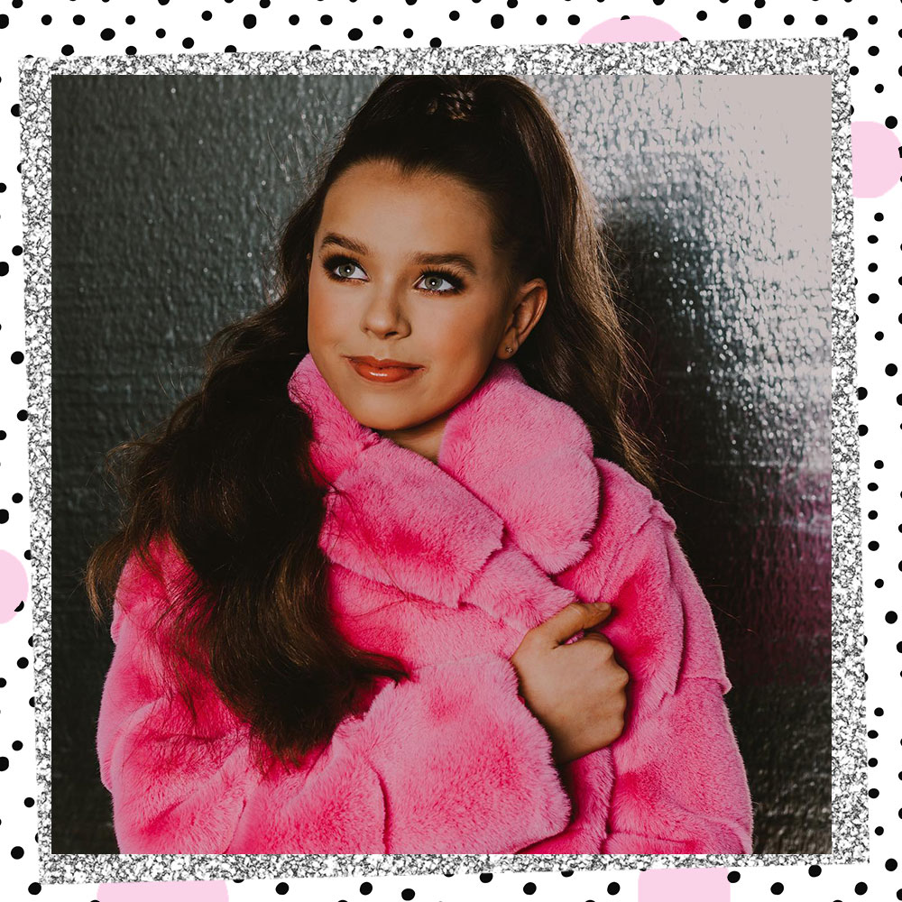 Tatum Brady poses in a hot pink fur coat and a high ponytail in front of a silver wall