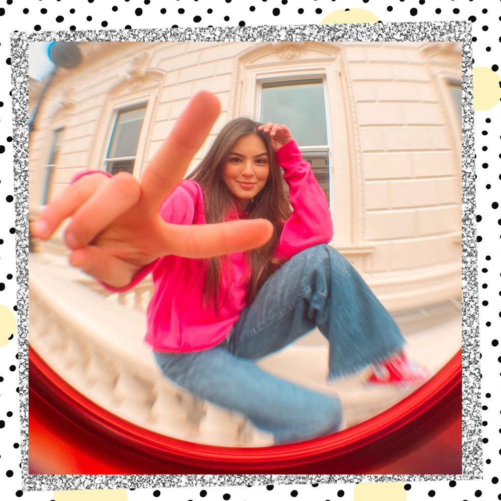 Fisheye lens captures Annissa Murad sitting on a balcony ledge giving a peace sign