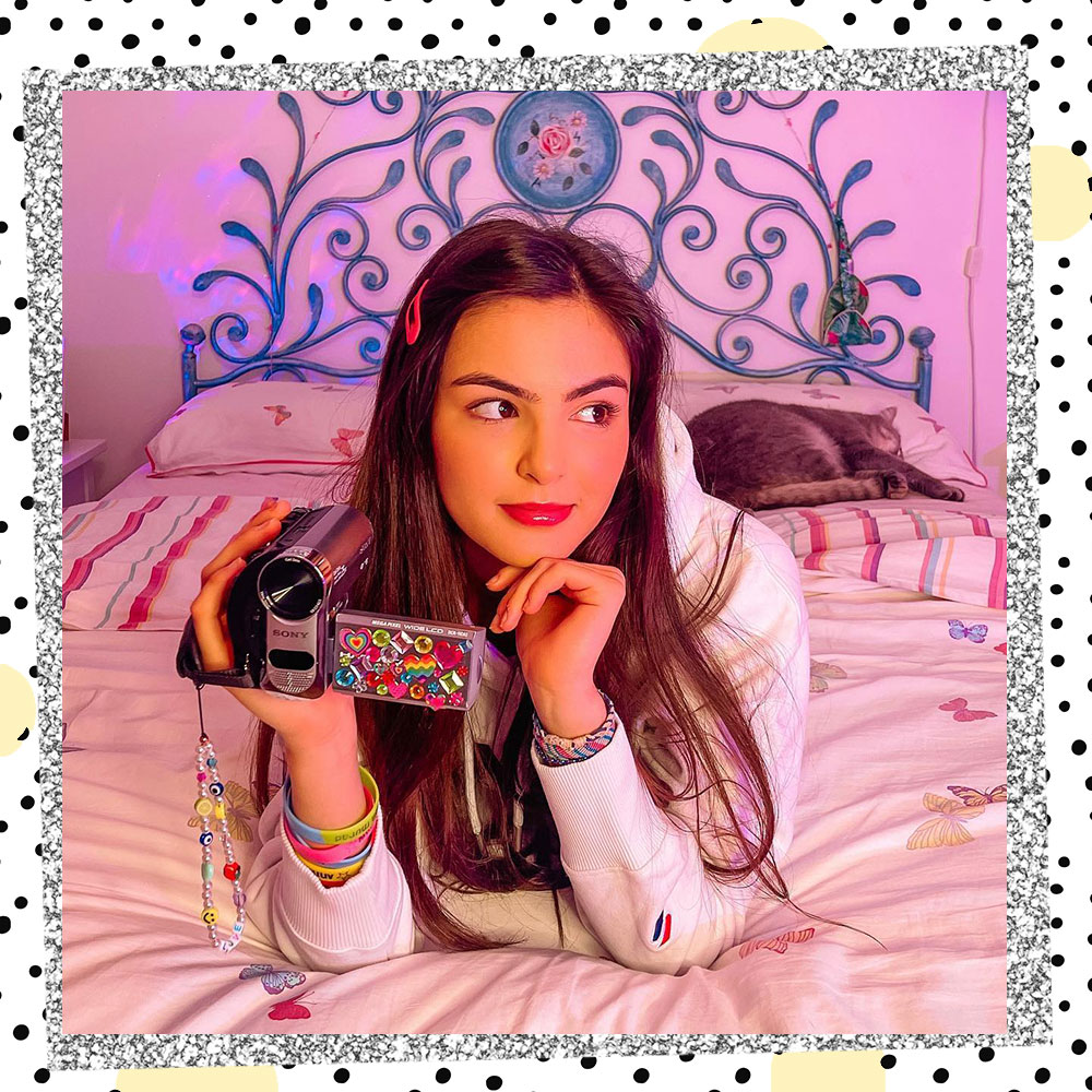 Annissa Murad laying on a bed holding a video camera covered in stickers