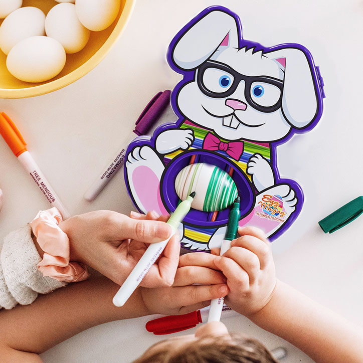 A Bunny Shaped Eggmazing Decorator sits on a table with an egg inside while kids use markers on it to create patterns