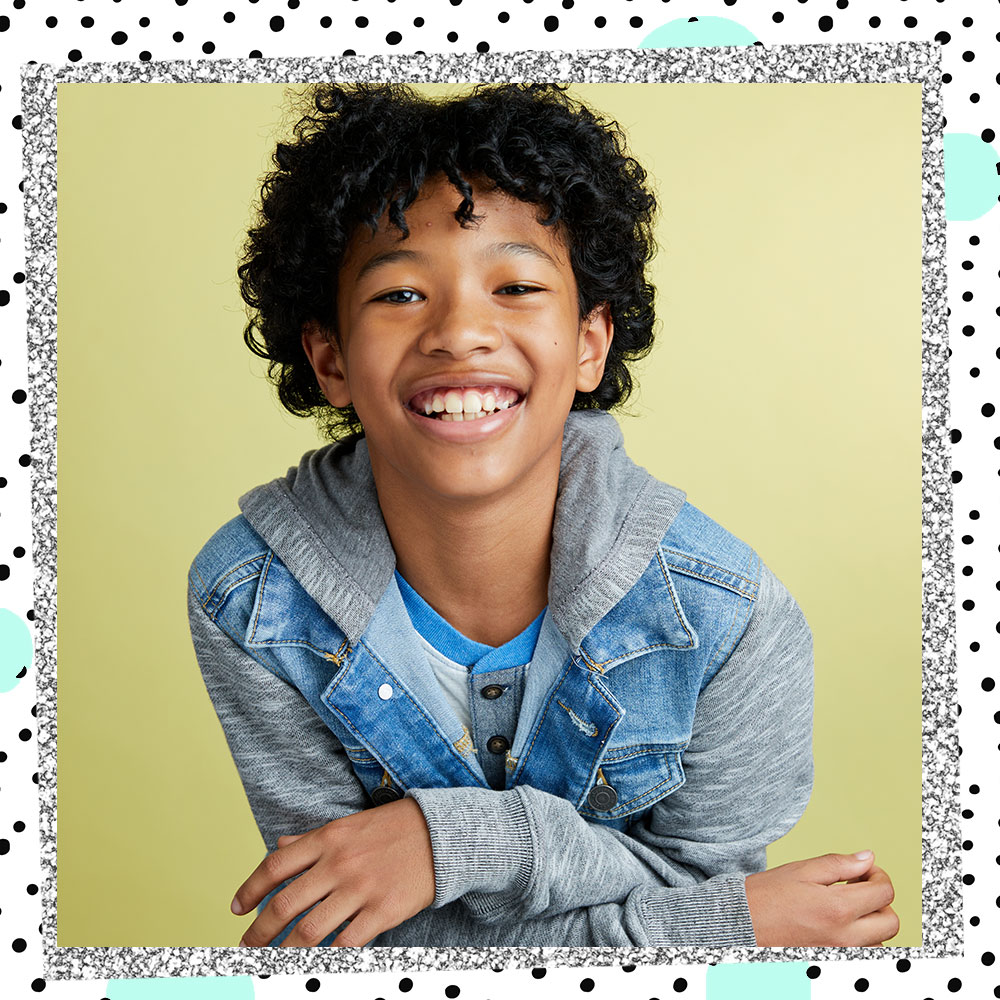 Jakari Fraser in a hooded denim jacket smiling in front of a pastel green backdrop