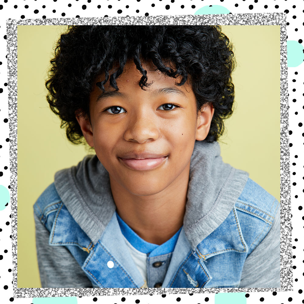 Closeup of Jakari Fraser in a hooded denim jacket smiling in front of a pastel green backdrop