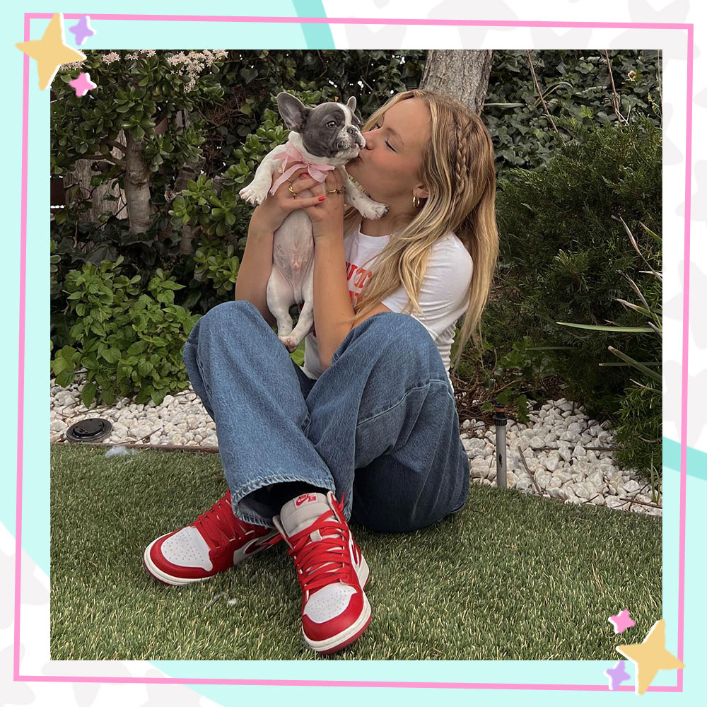 Pressley Hosbach in jeans and a tshirt, sitting in the grass holding and kissing her dog