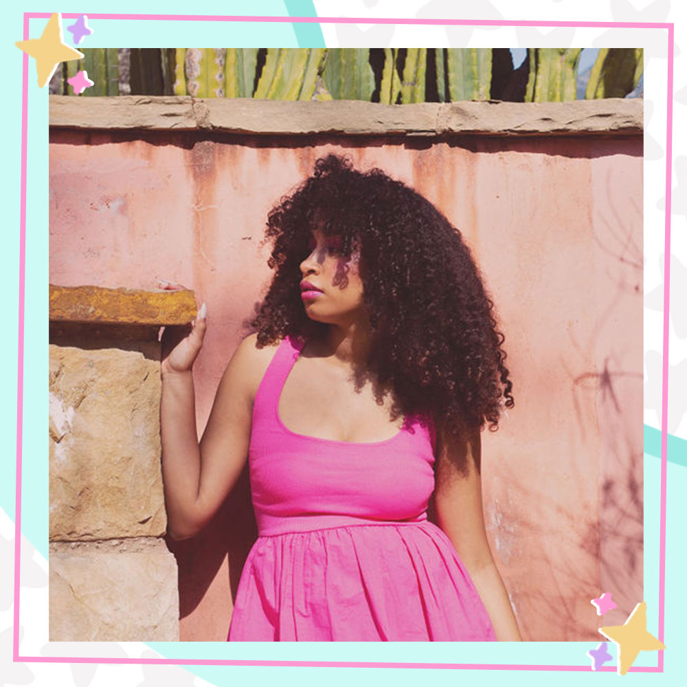 Jordyn Curet in a pink skater dress posing in front of a wall with cacti growing from it