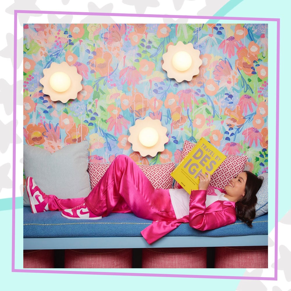 Annabelle Chang in a bright pink jogging suit and matching sneakers, laying down reading a book in the reading nook at her bookstore, Annabelle's Book Club LA